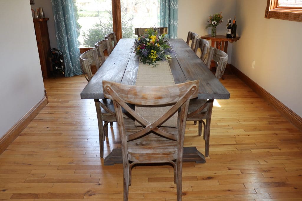Farmhouse Table with flowers in the middle sitting on a burlap runner.