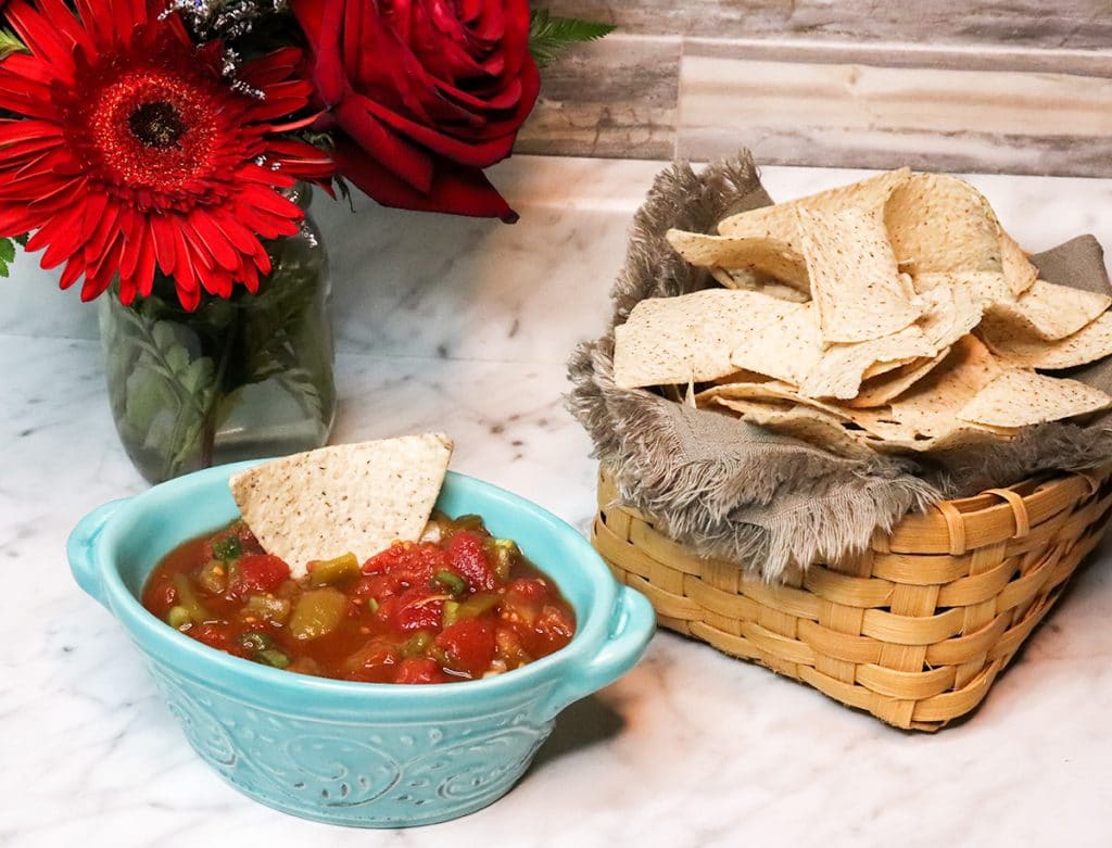 salsa in a bowl, tortilla chips in a basket, and red flowers