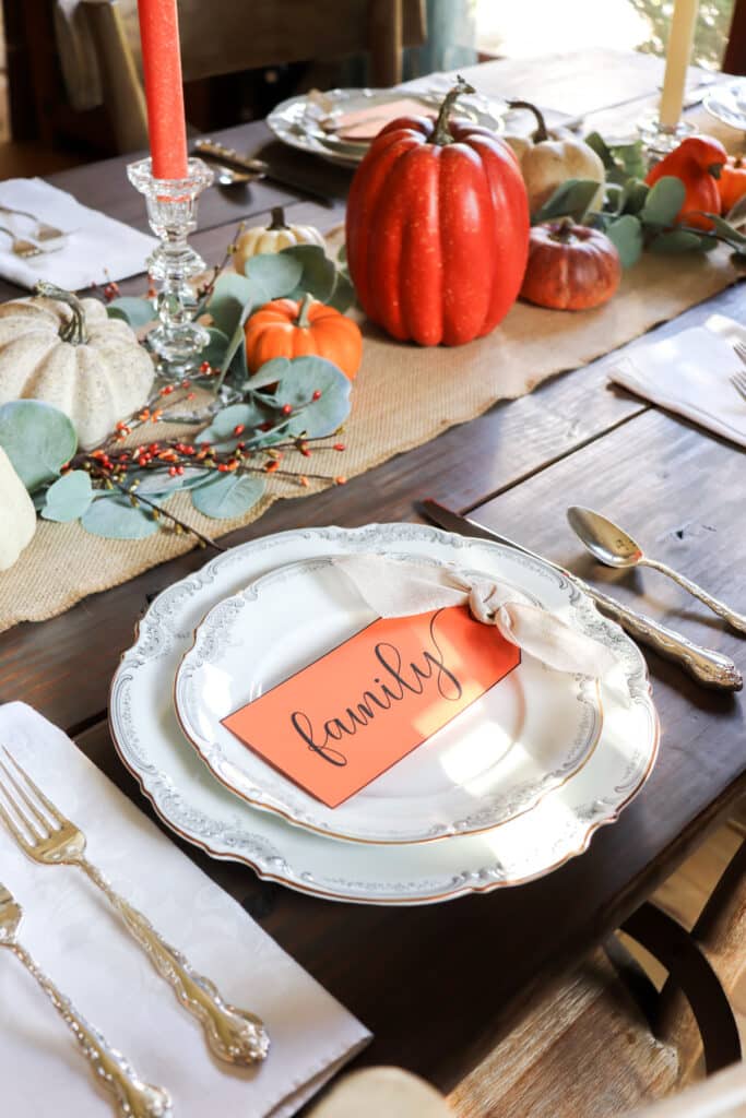 family tag on white china plate with pumpkins and faux berries behind it