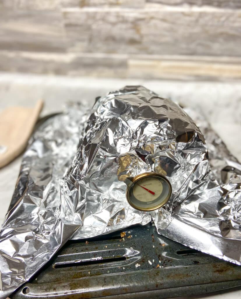 cooked meat covered in foil with thermometer showing