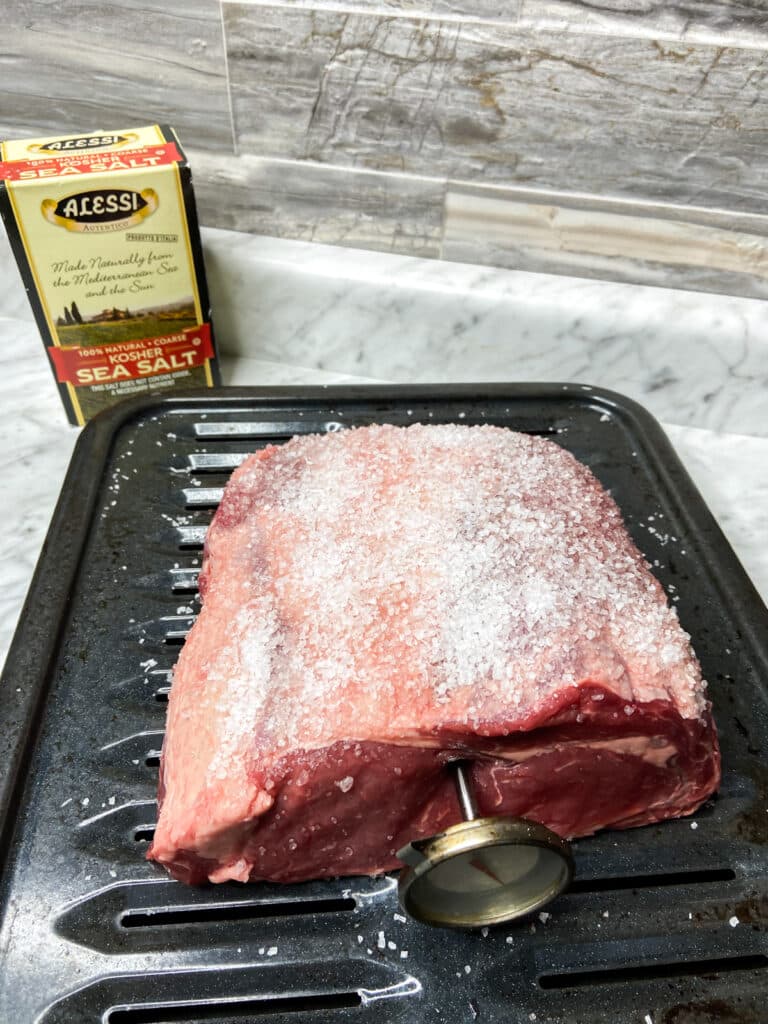 salt on top of rib eye roast, with thermometer in middle and salt sitting in background