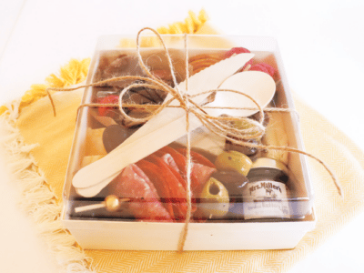 Charcuterie Box filled with meat, cheese, nuts, fruit, and tied with twine sitting on a yellow napkin.