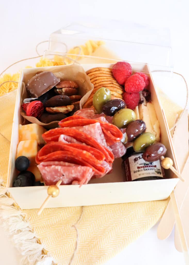 charcuterie box filled with meat, cheese, fruit, and olives sitting on a yellow napkin