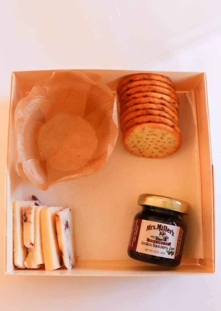 charcuterie box with cheese, jelly, crackers and an empty parchment cup