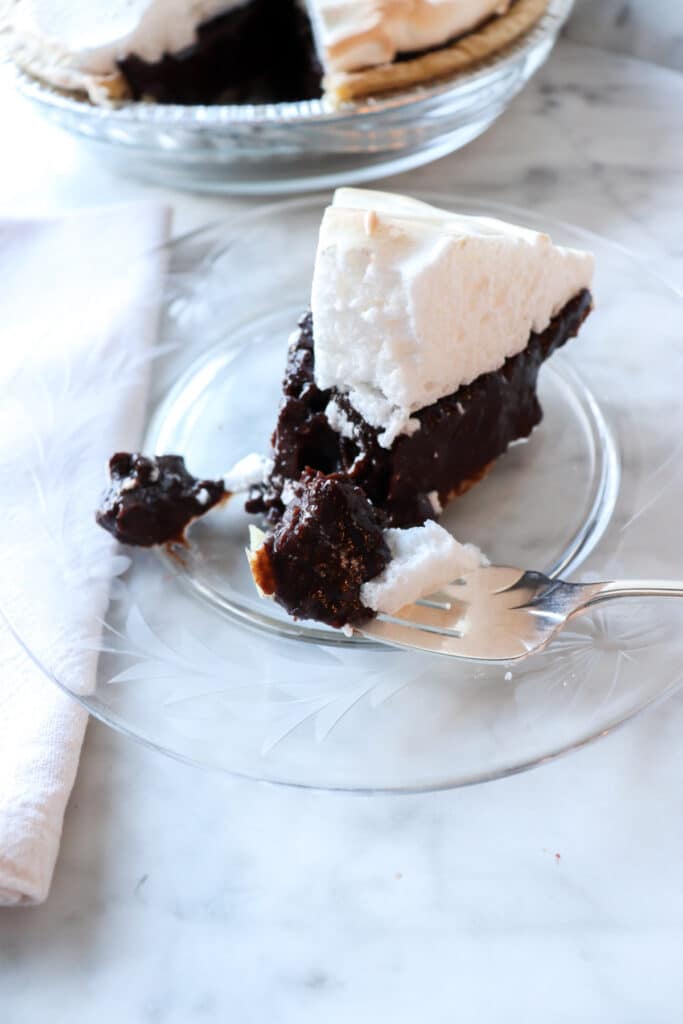 Slice of chocolate pie with meringue sitting on a clear plate.
