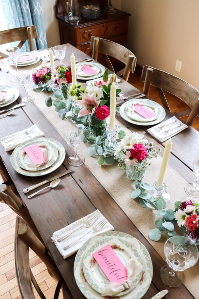 Mother's Day Table Decor Ideas showing place setting with china and silver flatware and flowers down the center with candlesticks.