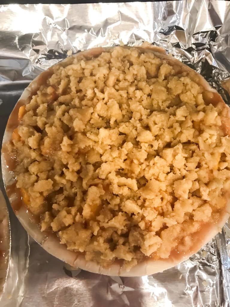 Crumble topping on top of peach filling before it goes into the oven.