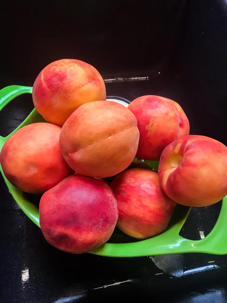 Fresh peaches after just being washed off and sitting in a strainer in the sink.