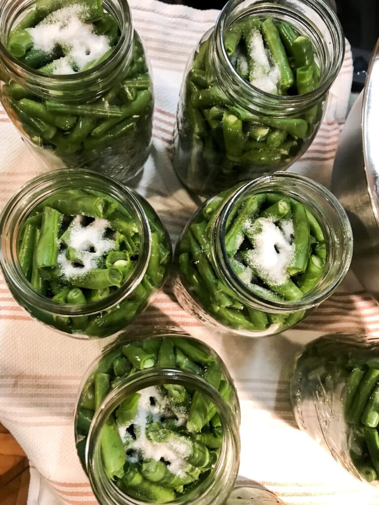 Jars packed with green beans and canning salt sprinkled on top.