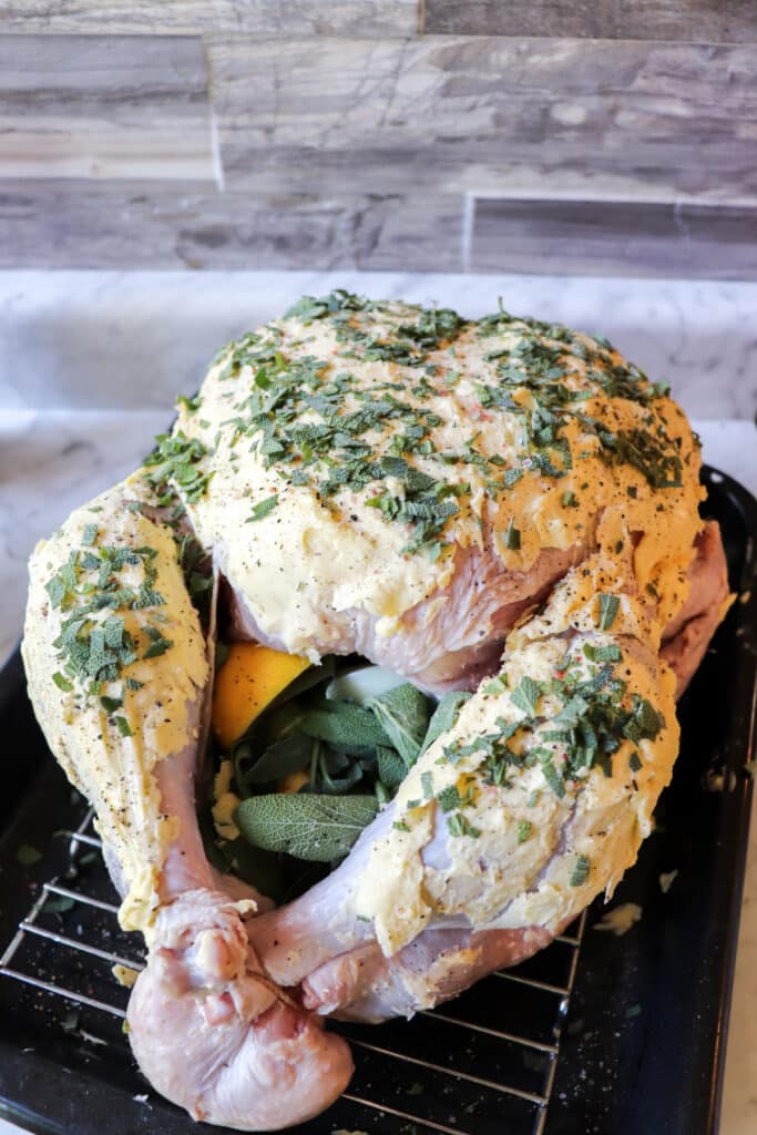 Turkey with butter and seasonings on top and cavity filled with lemons, onions, and sage.