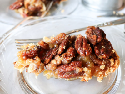 Slice of pecan pie on a clear plate with a fork.