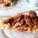 Slice of pecan pie on a clear plate with a fork.