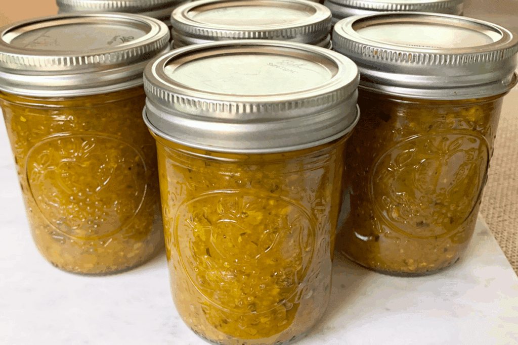 Three jars of canned zucchini relish sitting on a marble cutting board.
