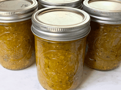 Three jars of canned zucchini relish sitting on a marble cutting board.