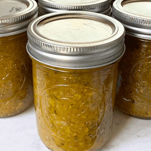 Three jars of canned zucchini relish sitting on a marble cutting board.