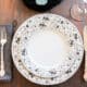 One place setting of china with a salad plate sitting on a dinner plate, a cloth napkin, and silver flatware.