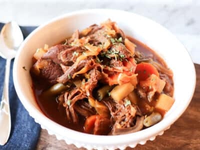 A bowl of stew on a wooden stand with a napkin and spoon on the side.