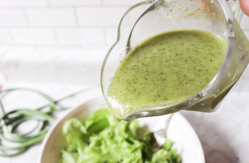 Pouring dressing onto a bowl of lettuce.