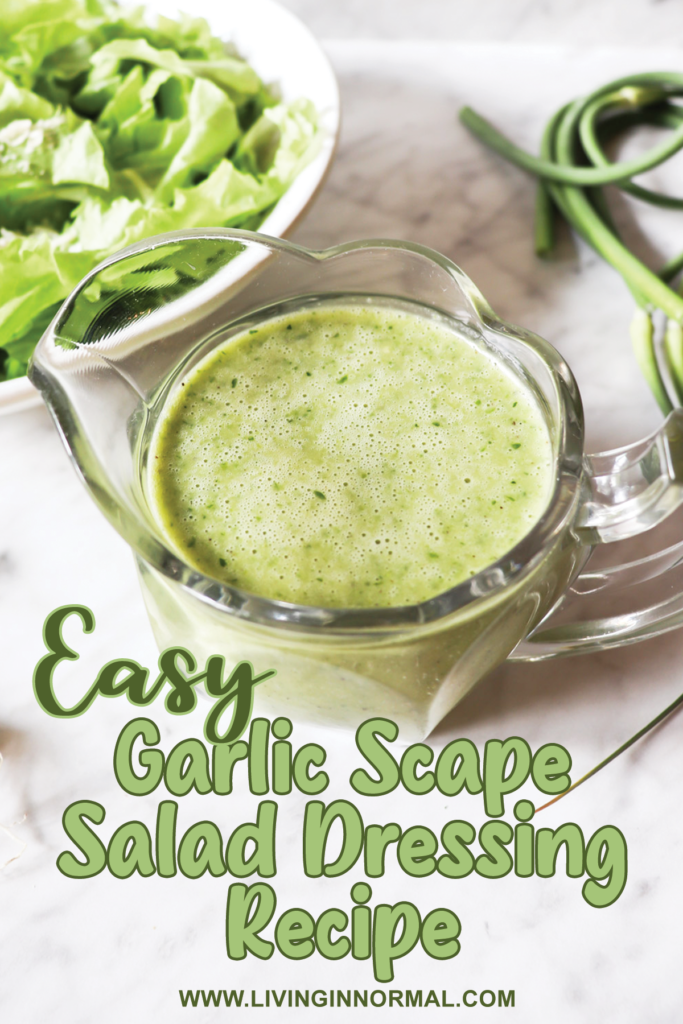Pinterest image of garlic scape dressing in a clear pitcher with lettuce in a bowl and garlic scapes and onions on the counter.