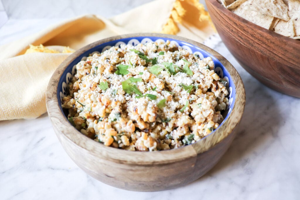 The dip in a wooden bowl with cheese and cilantro garnishing the top.