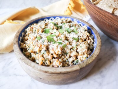 The dip in a wooden bowl with cheese and cilantro garnishing the top.