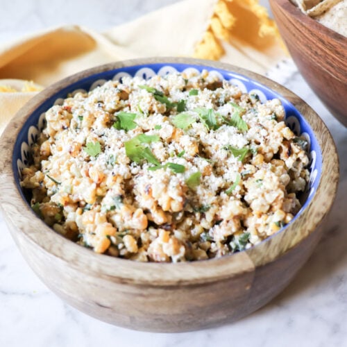 The dip in a wooden bowl with cheese and cilantro garnishing the top.