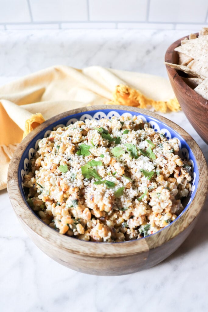 The dip in a wooden bowl with cheese and cilantro garnishing the top.