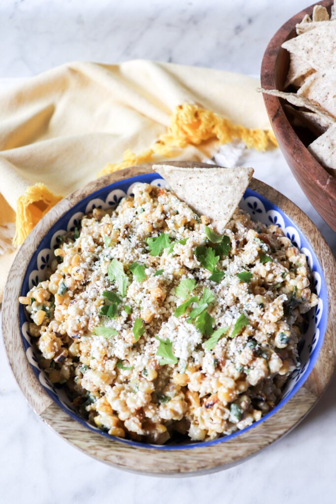The dip in a wooden bowl with cheese and cilantro garnishing the top.