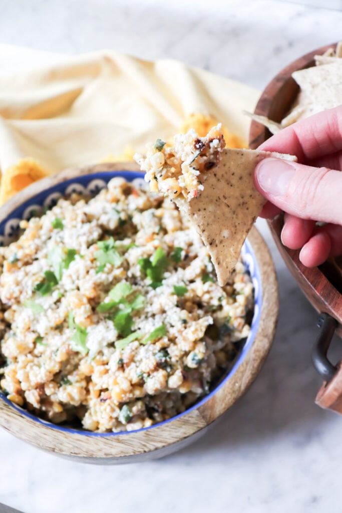 The dip in a wooden bowl with cheese and cilantro garnishing the top. And some dip on a chip.