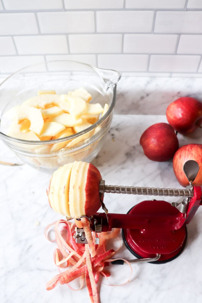 Apple peeler, corer, slicer on the counter with apples lying around.