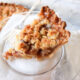 Slice of apple pie on a plate with the rest of the pie in the background.