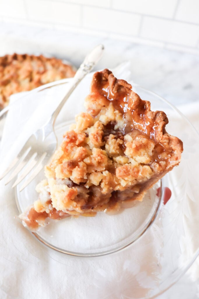 A slice of apple pie on a plate with the rest of the pie in the backgound.
